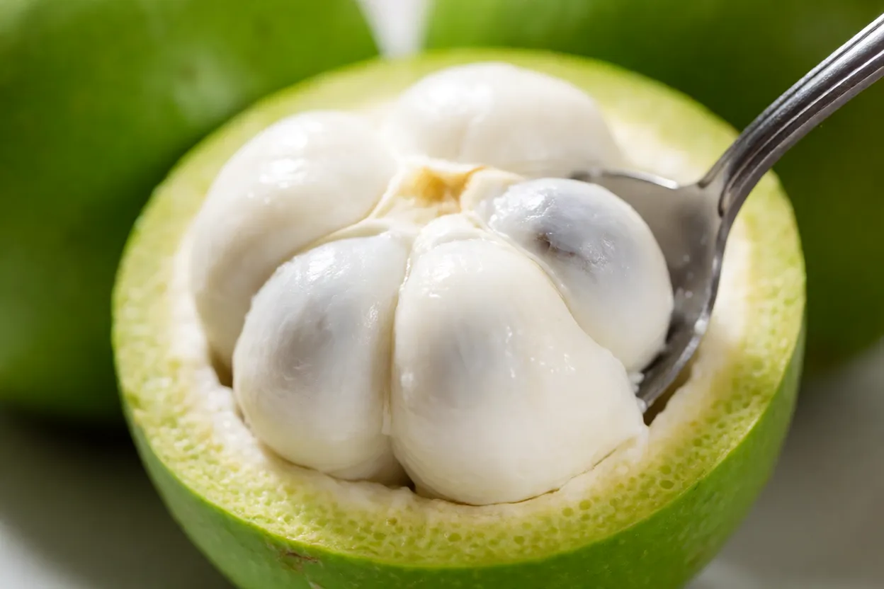 Mangostão cortado com colher retirando gomo de polpa branca